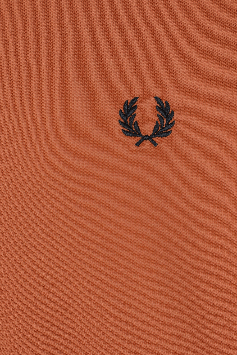 תמונת תקריב של חולצת פולו כתומה עם לוגו רקום FRED PERRY